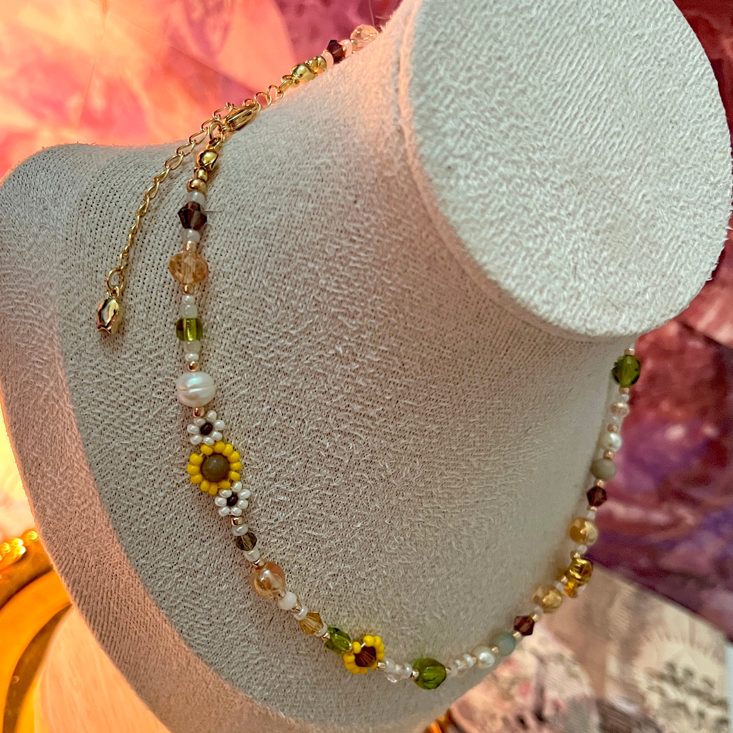 Necklace with sunflower pendants on a mannequin bust against a pink and orange gradient background
